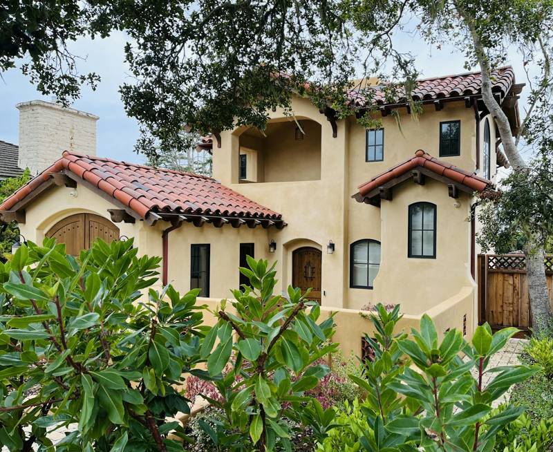 Casa de estuco estilo California con techo de teja roja entre árboles verdes