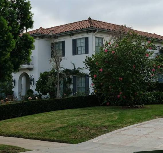 Casa blanca de dos pisos con techo de teja, césped y arbustos en flor